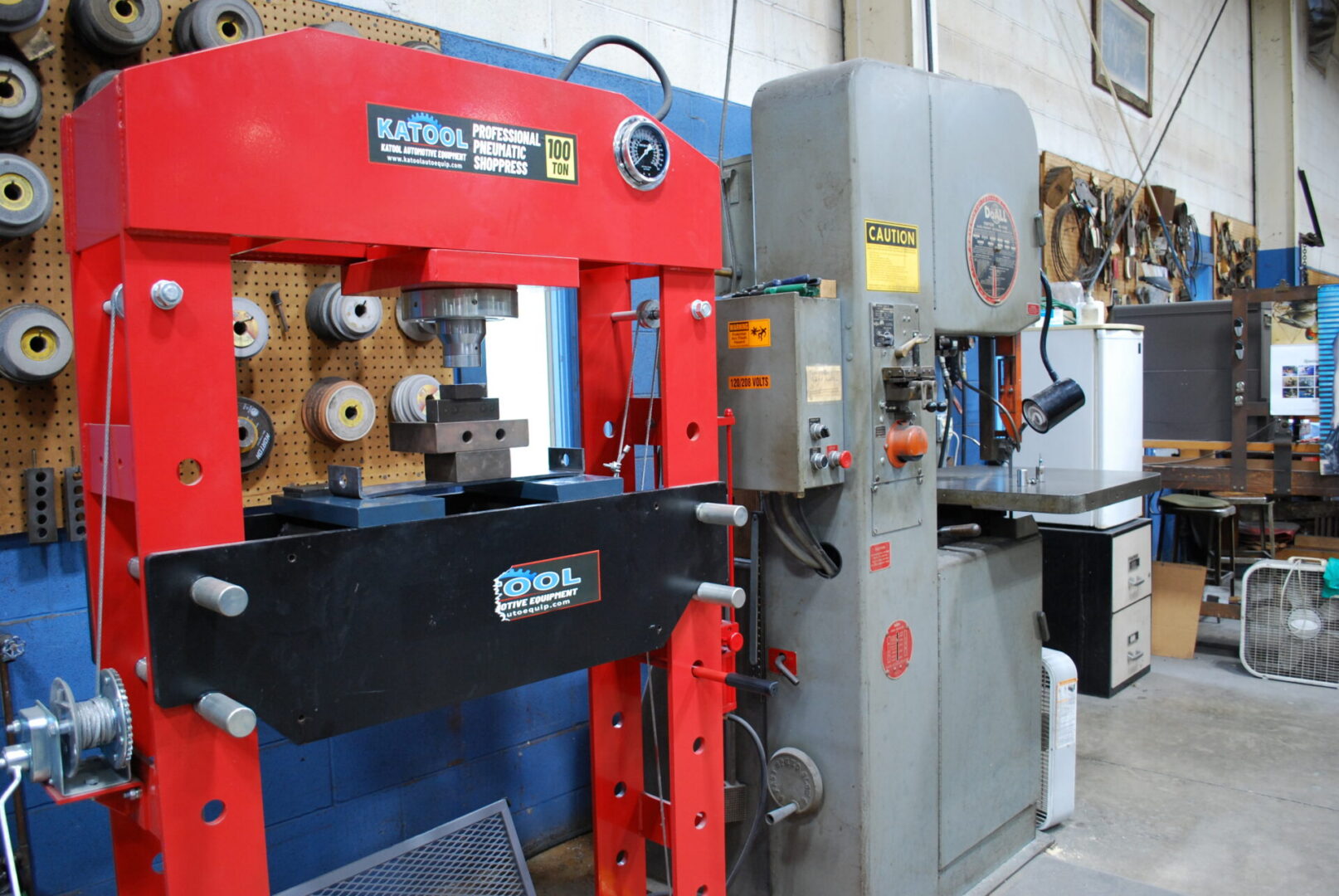 Red hydraulic press and metal bandsaw in workshop